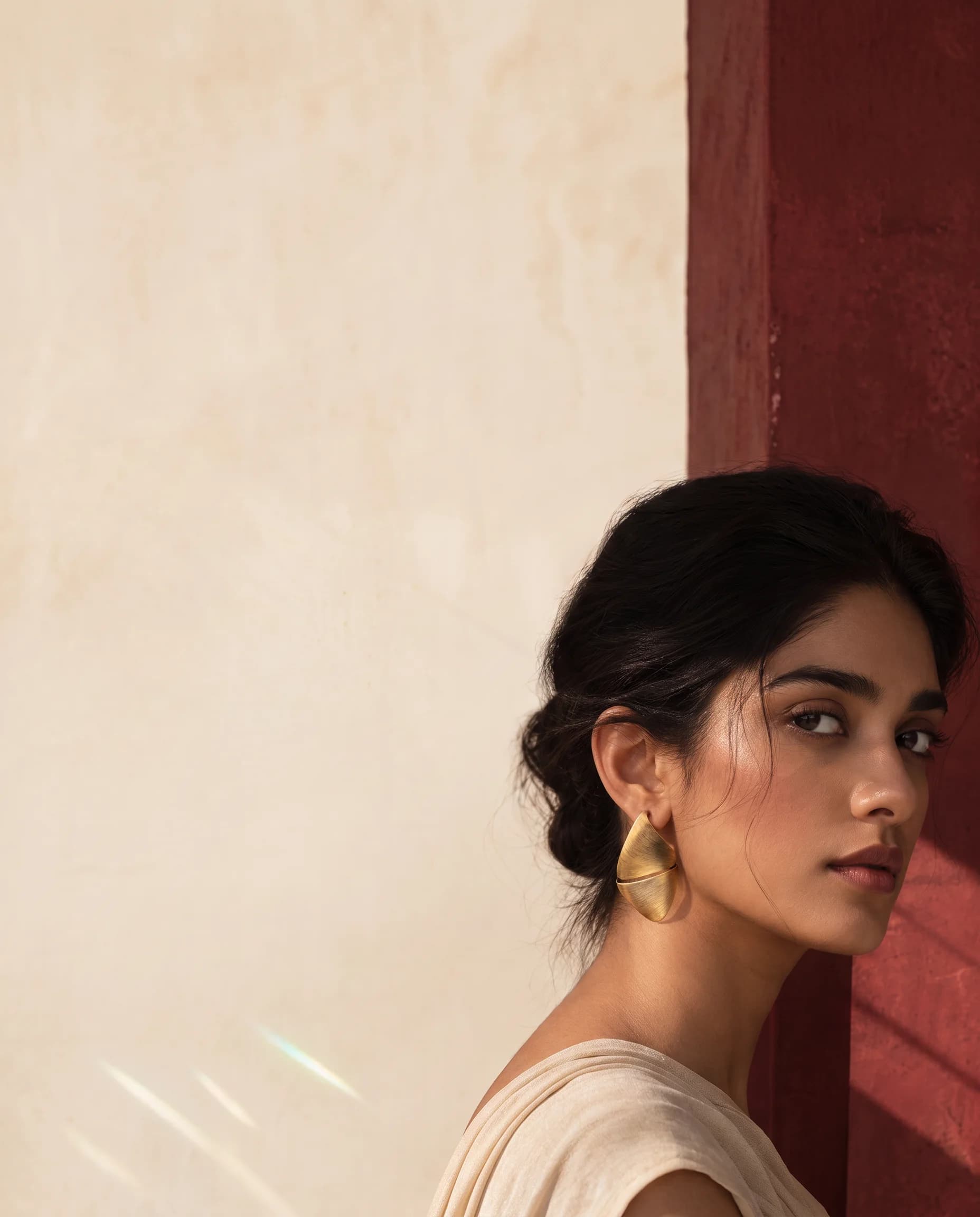 Woman in profile against an ivory and deep-red wall, wearing a brushed gold leaf earring