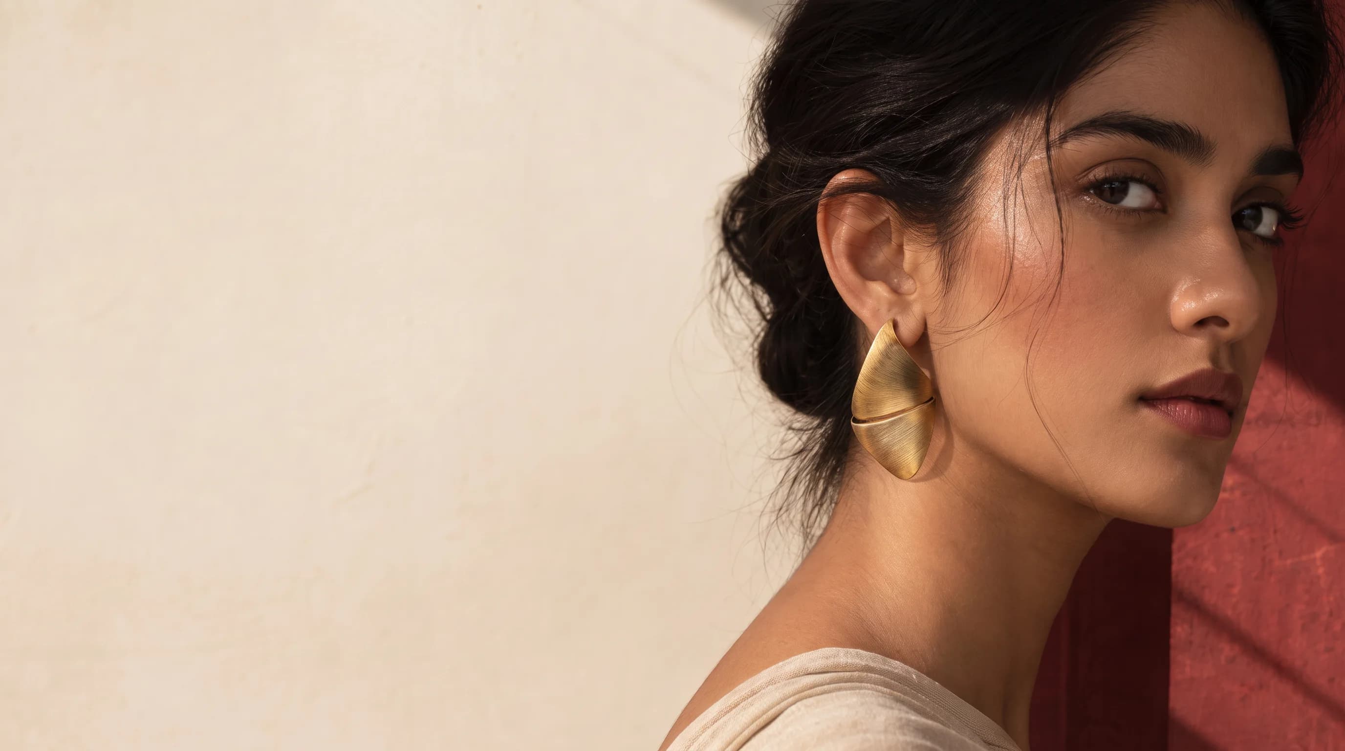 Woman in profile against an ivory and deep-red wall, wearing a brushed gold leaf earring