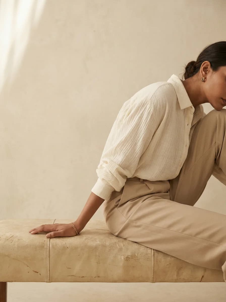 Woman in an ivory cotton shirt wearing small gold huggie hoops and a fine chain bracelet